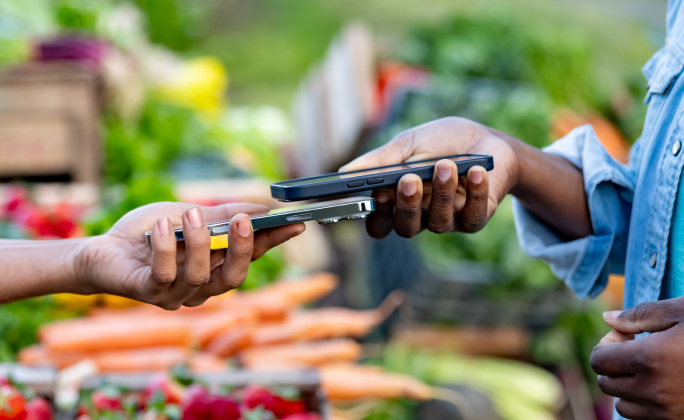 Cliente paga contactless con smartphone a un venditore in un negozio di frutta e verdura.
