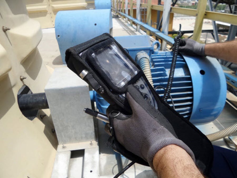 A technician holding a manual vibration meter on a motor.