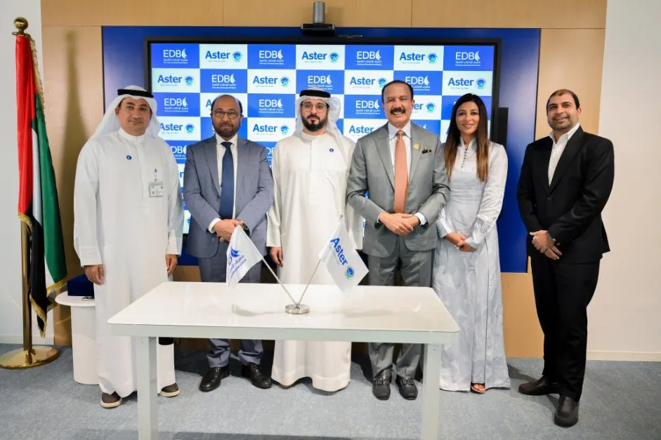 Six people standing at a signing-ceremony table in front of an Aster-branded backdrop, with a UAE flag alongside