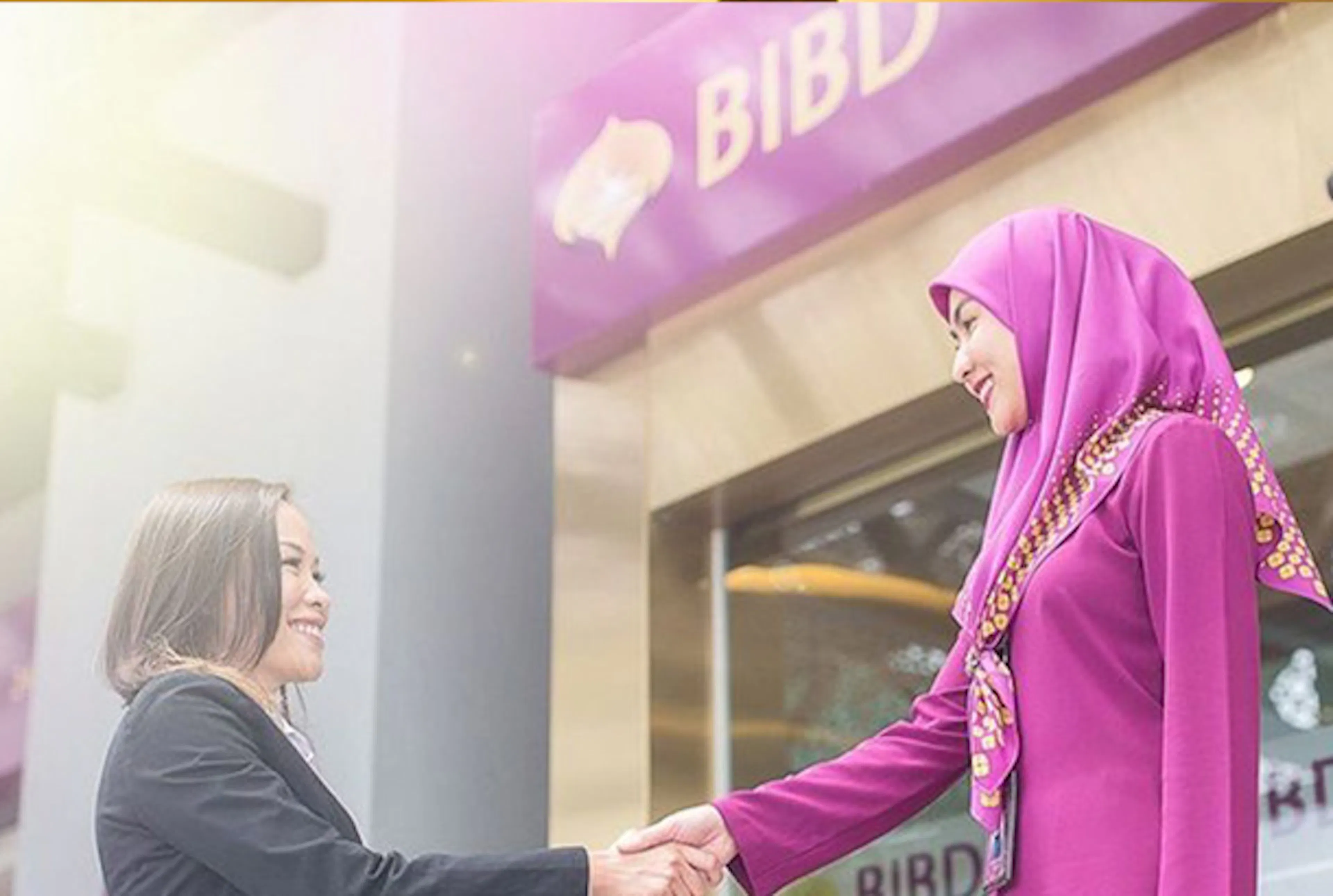 Two women shaking hands outside Bank Islam Brunei Darussalam bank