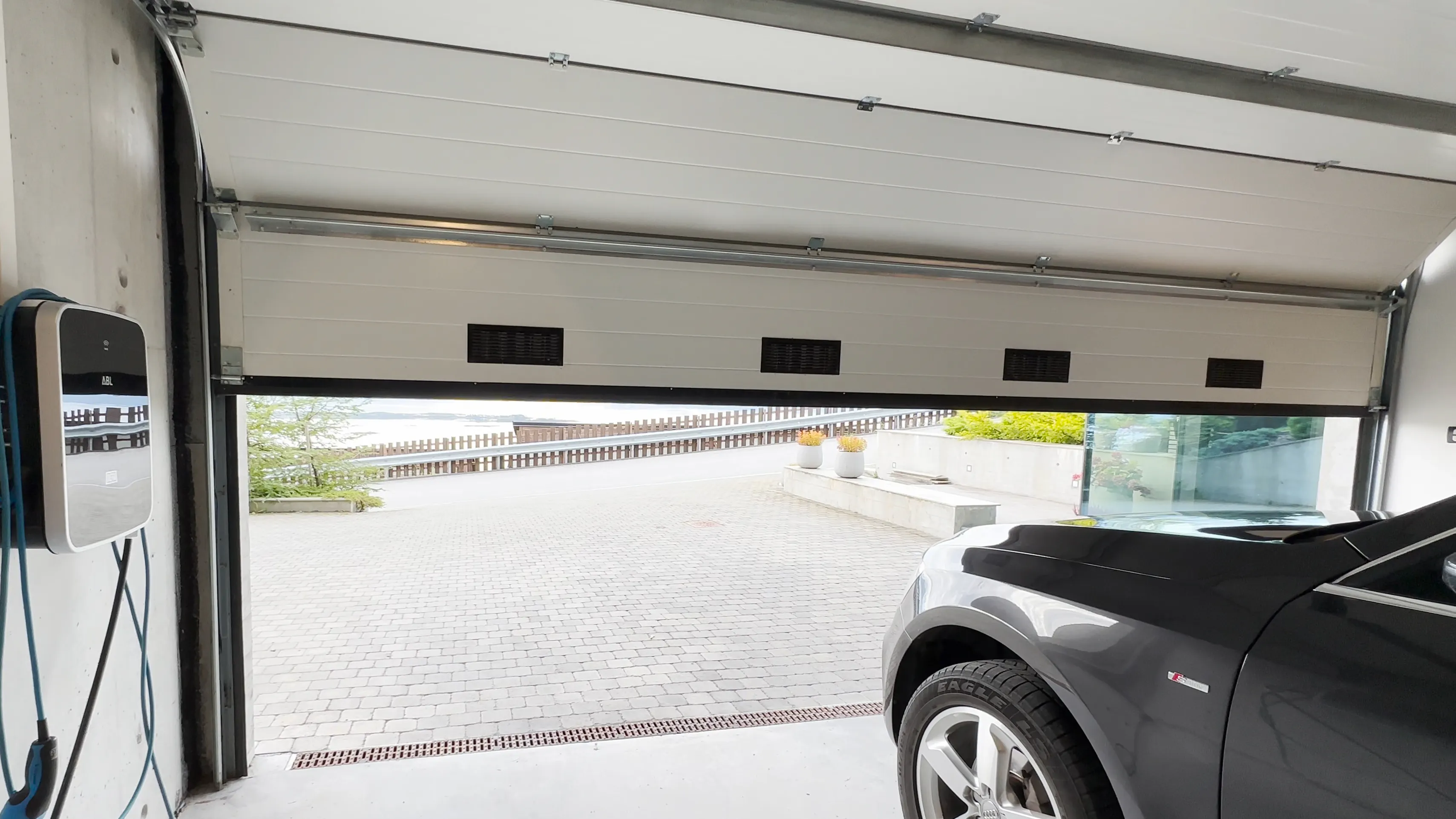 Rullegardin senket delvis over et bredt vindusfelt, demper lys og skjuler utsikt. Montert i moderne interiør/showroom med hvitt tak, synlige skinner og glasspartier.