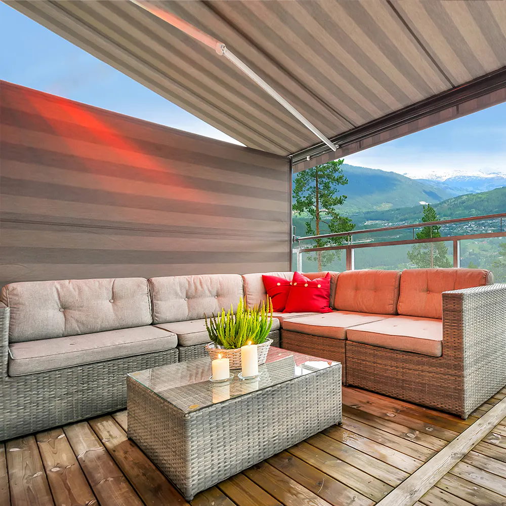 Markise og nedsenket screenside skjuler terrasse; flettet hjørnesofa med røde puter og glassbord med plante og telys på treterrasse, glassrekkverk og fjellutsikt.
