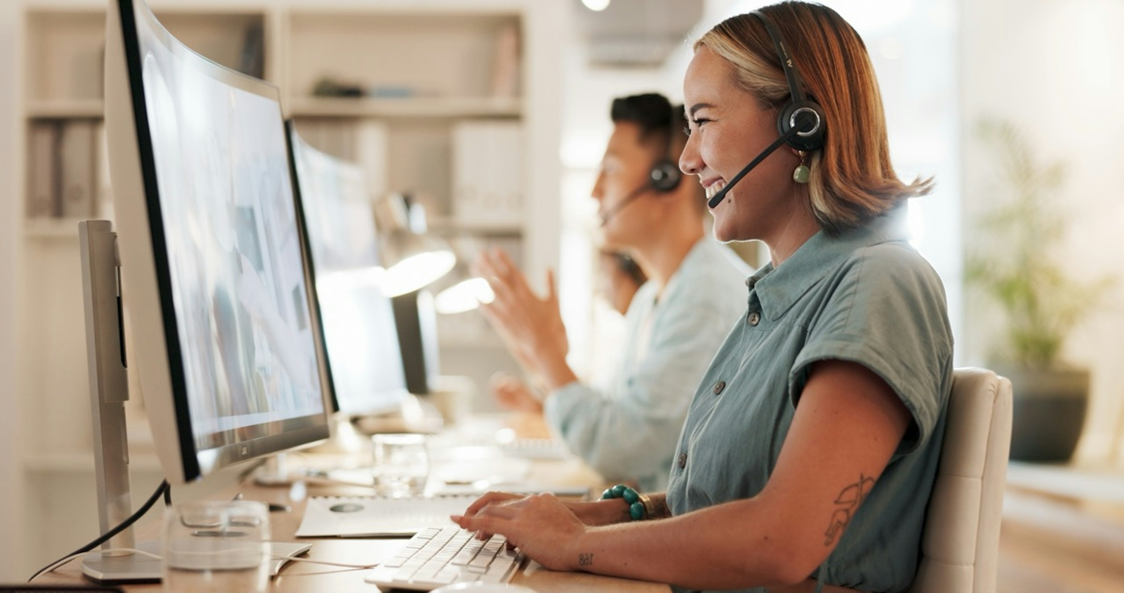 Customer support agents wearing headsets work at desktop computers in a modern office, assisting customers through live calls