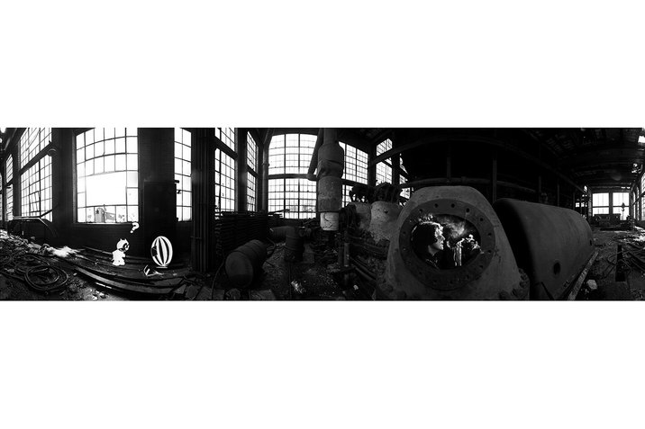 A black and white image of an abandoned space full of cables, oil drums and tubes. On the left collaged the cartoon character doraemon looks at a ball with a question mark above its head. On the opposite end of the panorama image, is a collaged image of Paul Mccartney en face smoking. 
