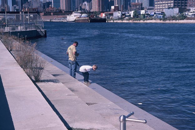 Two figures stand on stairs leading to the water. The smallest figure dressed in a white shirt crouches looking at the water's surface.