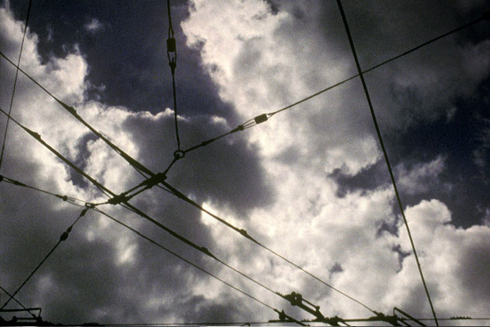 An image of many interconnected wires against a dark cloudy sky.