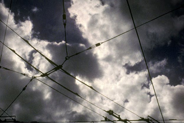 An image of many interconnected wires against a dark cloudy sky.