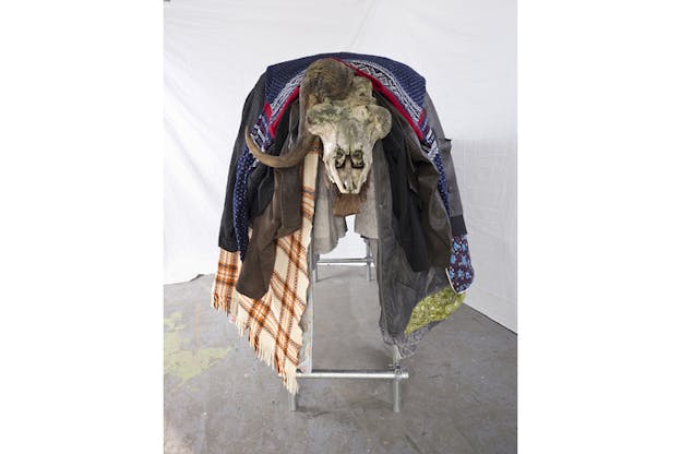 The skull of a buffalo with only one horned is situated on a metallic chair covered by multi-patterned materials. 