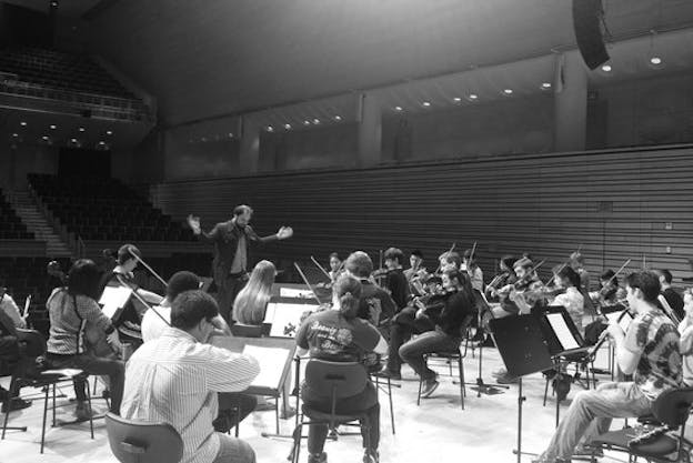 Black and white photograph of Layton conducting an orchestra in an audience-less auditorium.