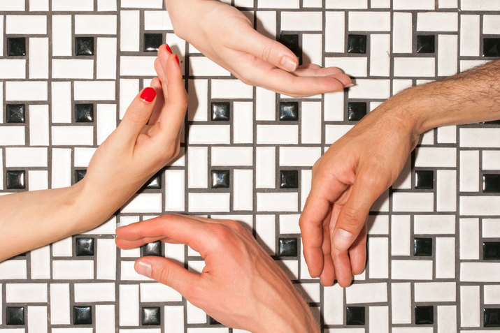 Four hands and wrists angle towards and away each other, forming a diamond-like shape against black and white geometric patterned tile.