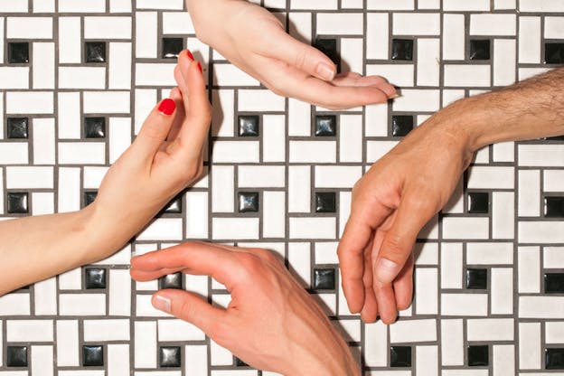 Four hands and wrists angle towards and away each other, forming a diamond-like shape against black and white geometric patterned tile.