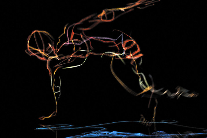 A sketch of a human figure lunging towards the left on one hand and one knee is projected onto an otherwise black space. The figure is given shape with lines in orange, gold, silver, and lavendar. A cluster of blue lines is in the bottom of the scene. 