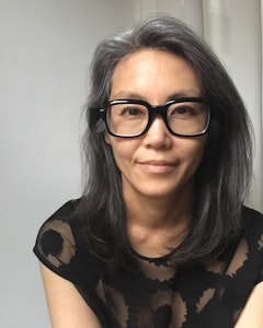 Portrait of Kay Takeda wearing a black shirt and thick black-rimmed glasses, he hair sits on top of her shoulders