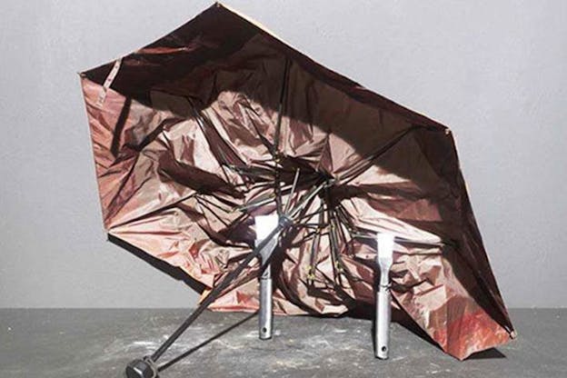 Close-up of a reddish brown crumpled umbrella resting on its side and upheld by two metal objects. 