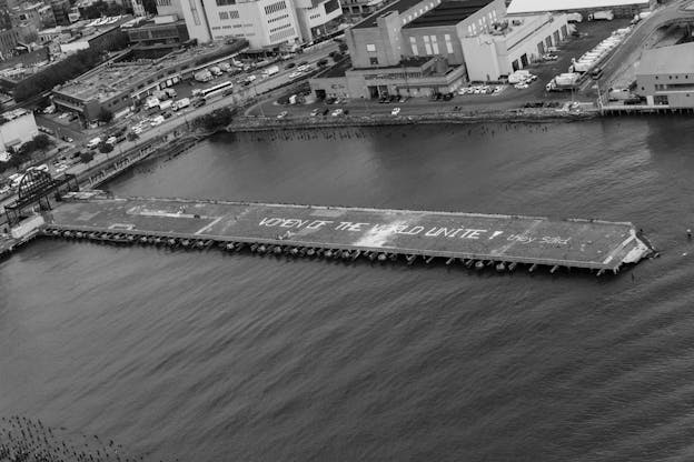 A black and white aerial shot of Pier 54 with the pier appearing a horizontal line across the center of the frame . On the pier the words 