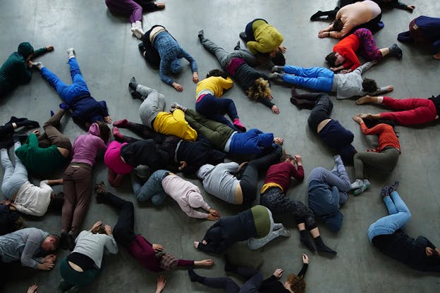Eagle view image of people in colorful clothing laying down on a gray floor in a clutter.