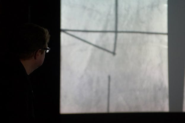 A person on the left side stares at a black and white projection showing a few lines intersecting one another.