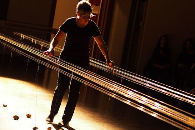 Fullman in a dimly lit room plays the long string instrument: dozens of long, fine wires suspended at waist-height.