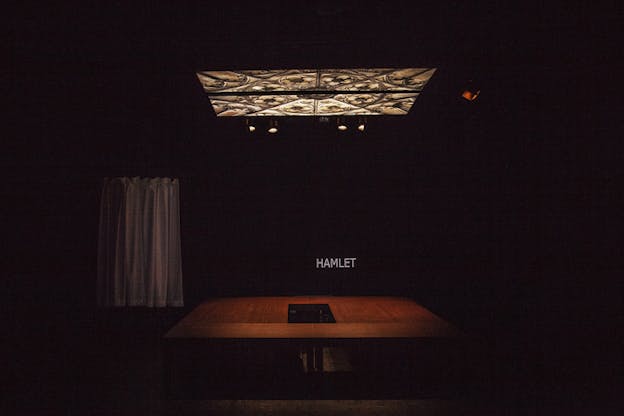 A stage with black surroundings. On its wall a projection with a dark background and the word 