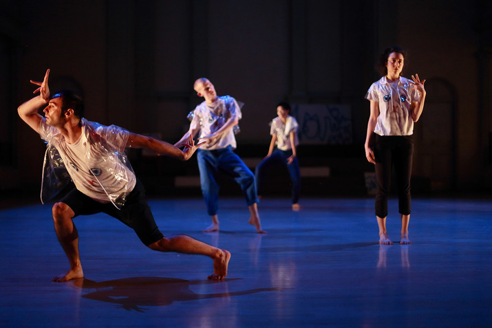 Four performers on stage freeze in different poses while in a zic-zac formation. They all wear white t-shirts a cat's face and blue eyes printed on them.