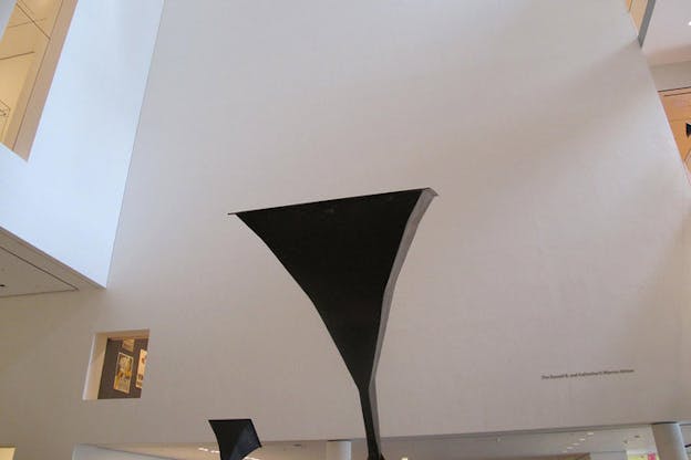 Low-angle shot of a tall blank wall with a triangular black sculpture shaped like a flattened phonograph. 