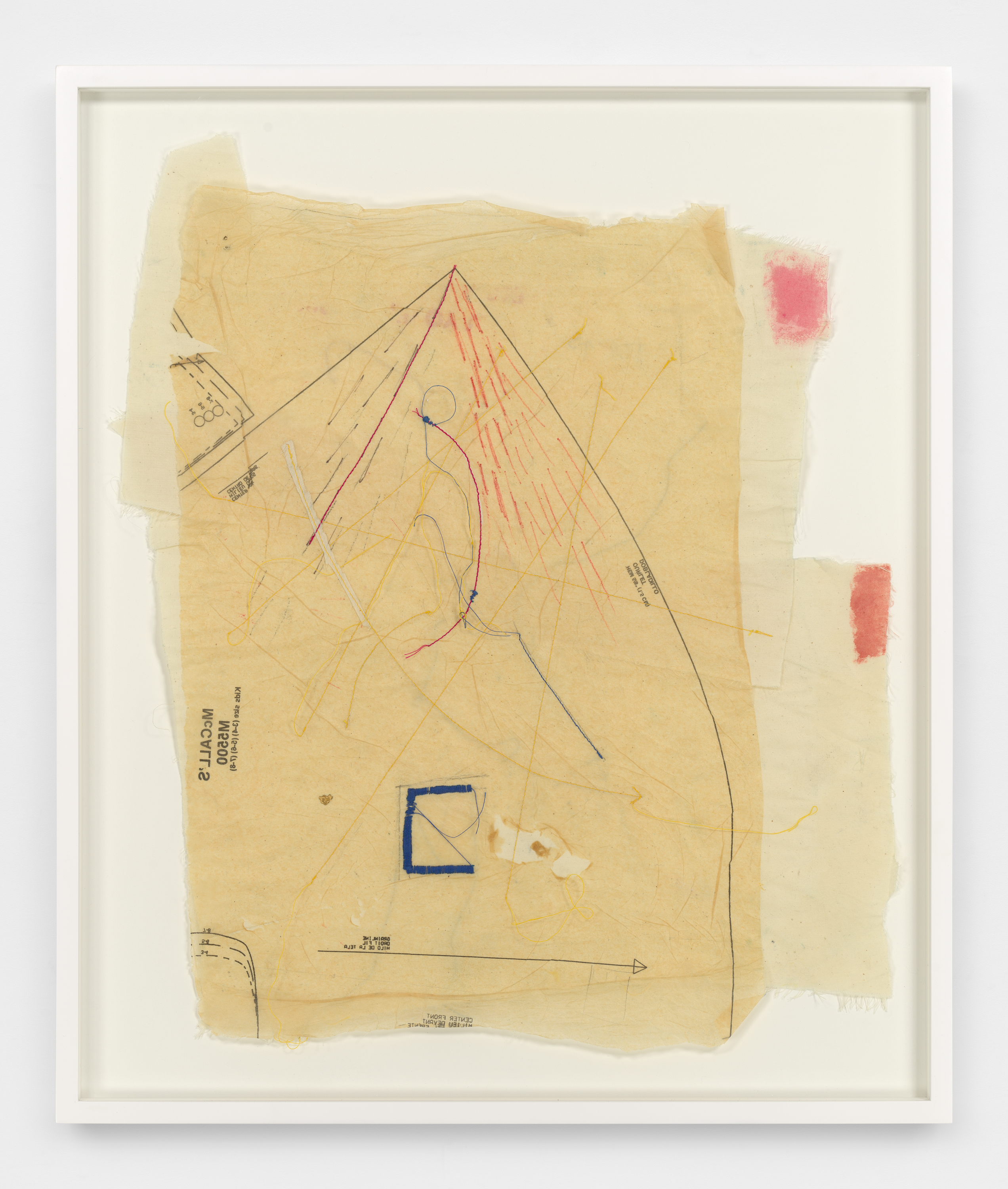 Within a frame, two pieces of off white fabric are layered below a piece of translucent, tan, sewing pattern paper. On the pattern paper are fine black pattern outlines and instructions in small black print, and embroidered dashes and rays in gray, magenta, yellow, and orange thread. 