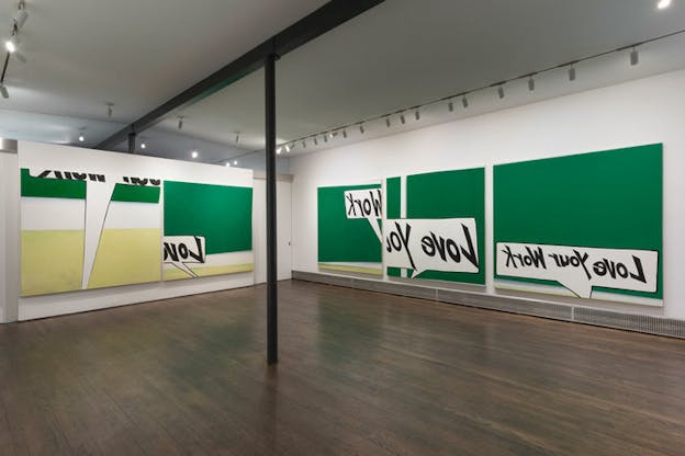 An exhibition photograph with three large green canvases hung on the right wall and two green canvases hung on the left wall. The canvases show a varity of speech bubbles with snippets of the phrase 