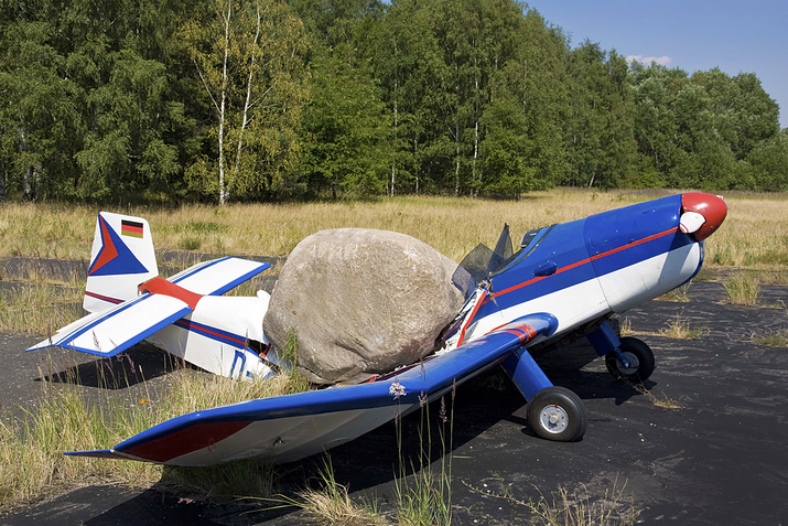A gray boulder crashed down on the roof of a blue and white airplane, breaking it in the middle.
