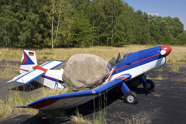 A gray boulder crashed down on the roof of a blue and white airplane, breaking it in the middle.
