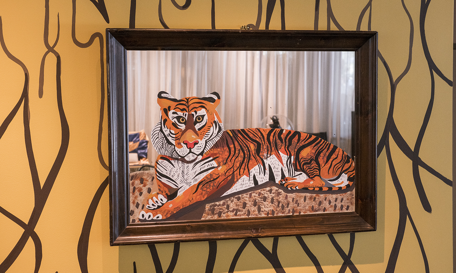 A framed painting of a tiger is hung on an orange wall painted with black abstract lines.