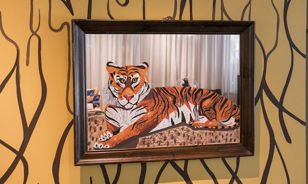 A framed painting of a tiger is hung on an orange wall painted with black abstract lines.