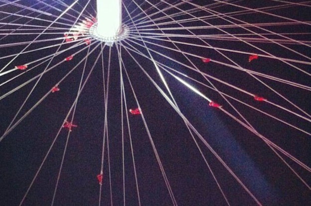 Multiple cables that support performers clad in black meet in the middle of a white column.