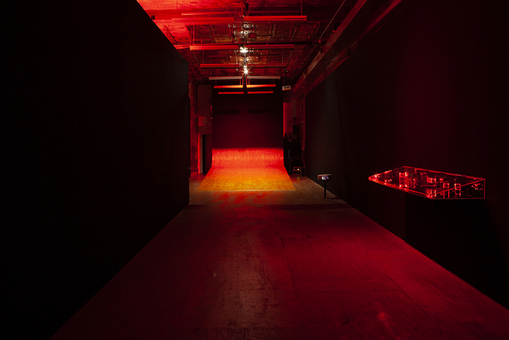 A red dimly lit hallway leading to its end in a wire made ramp against a dark wall.