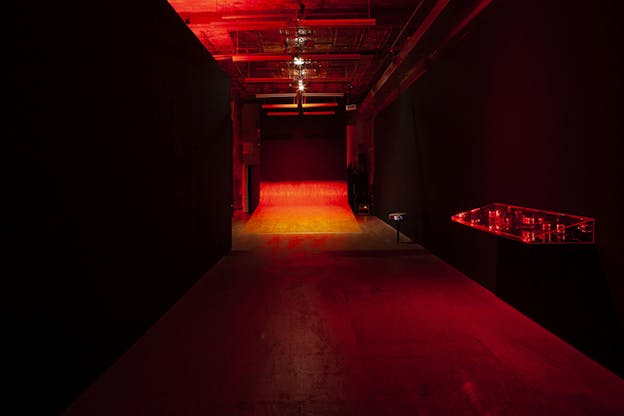 A red dimly lit hallway leading to its end in a wire made ramp against a dark wall.