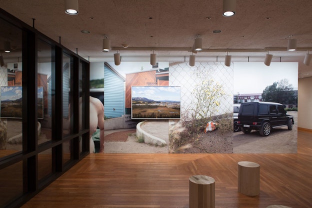 A framed photograph of a rural valley overlaps four juxtaposed images of a parked jeep, a yellow flower beside a wire fence, a house, and a person's bare chest. 