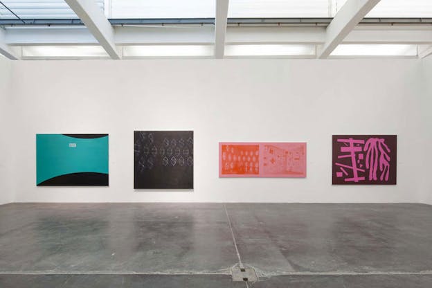 Four abstract paintings on center wall, from left to right a curving turquoise cuts through black, chalky white octagon sketches against dark gray, a pink and red screenprint of octagonal shapes and a wall with posters, and squiggly pink shapes against brown paint.