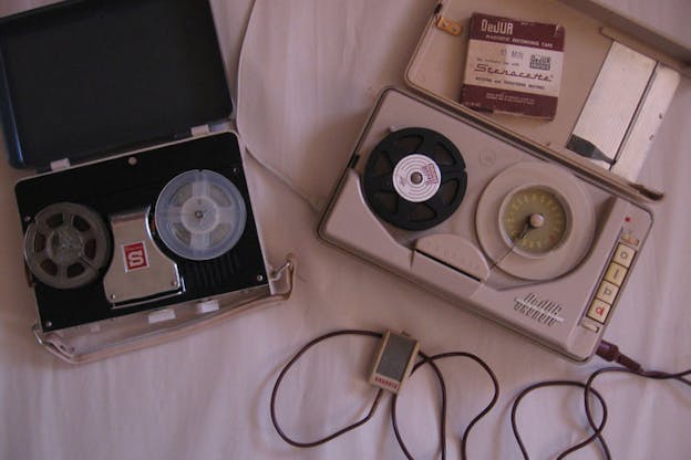 Vintage recording instruments, resembling tape cassettes, photographed against a bed sheet.