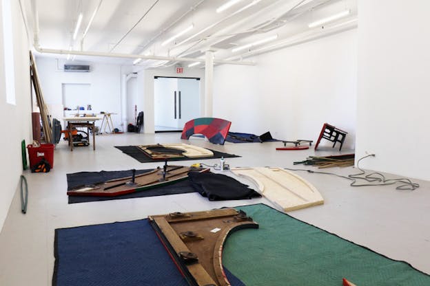 A white room hosts different wooden cut outs laying on the floor on top of blue and green sheets.