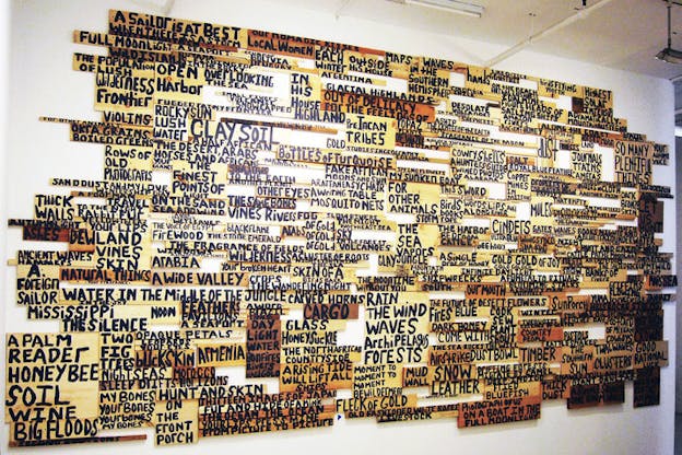 Wall installation of collaged wooden planks with words and sentences such as 