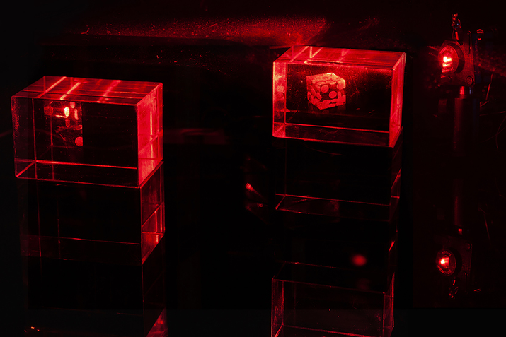 A pair of dice sit separated inside transparent boxes their surrounding dark illuminated by an intense red light.