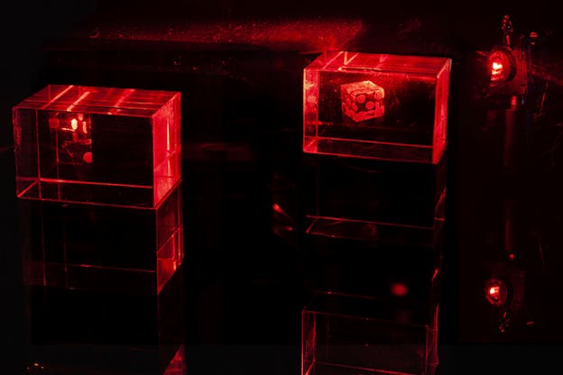 A pair of dice sit separated inside transparent boxes their surrounding dark illuminated by an intense red light.