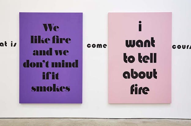 Two canvases are hung from a white wall. On the left, a purple canvas with black text reads: 
