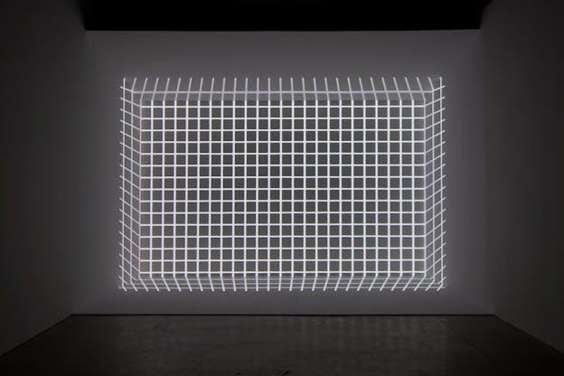 At the far wall of a grey room, a grid made of light is projected in such a way that creates the optical illusion of the grid being a 3D cube.
