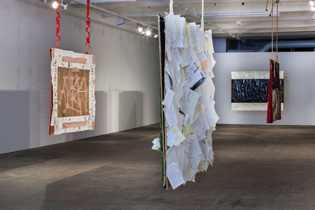 Gallery installation of four hanging quilts, one arranged with loosely bound pages, one with a dark blue spiral diagram, one with a straight-line diagram, and one with red cloth and mixed-fabric. 