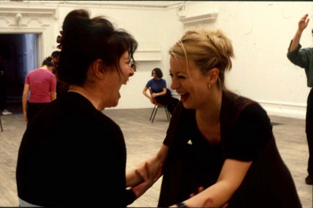 Photograph of two people looking directly at each other, their faces close and holding each others forearms while laughing.