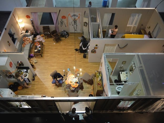 An eagle view of an apartment with a living room, bathroom, kitchen and bedroom. Various people can be seen doing different tasks.