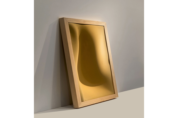 A mustard yellow canvas with a light wooden frame leans against a wall. On some areas the canvas protrudes upwards creating a wavy movement.