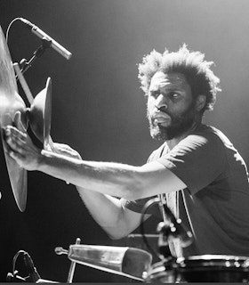 Black and white portrait of Marshall Trammell playing the drums. Bright white light illuminates him from the left.