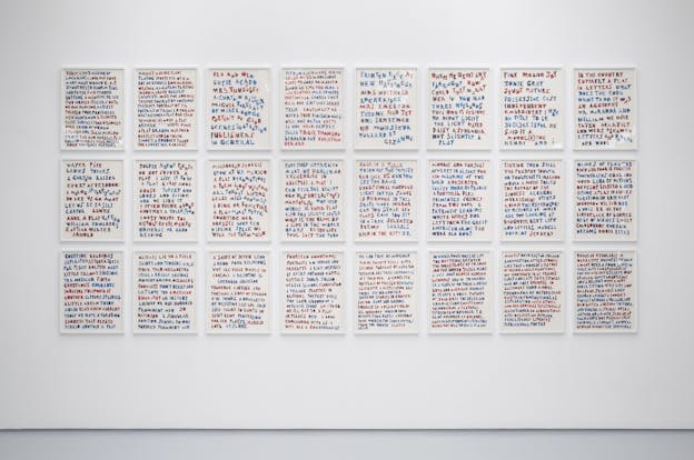 A white gallery wall with 24 framed images arranged 8 by 3. Each image shows text written in red and blue marbled letters with a white background. 