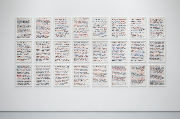 A white gallery wall with 24 framed images arranged 8 by 3. Each image shows text written in red and blue marbled letters with a white background. 